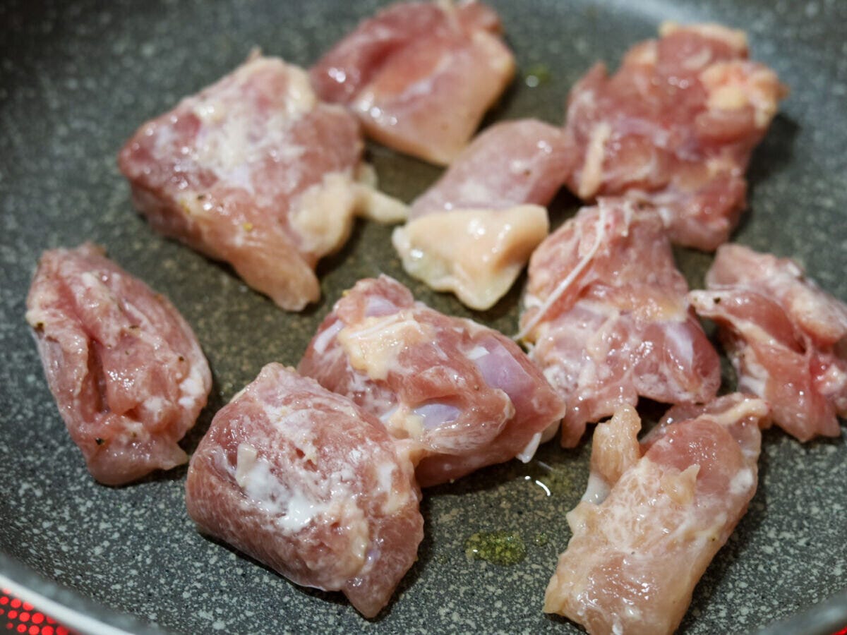 鶏もも肉を皮目から焼く工程 グレーのフライパンに片栗粉をまぶした鶏もも肉を皮目から並べて焼きはじめた様子