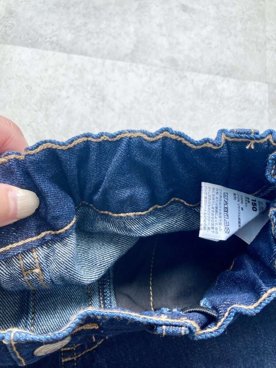 デニムのウエスト内側のゴムとタグを指でつまんで見せている