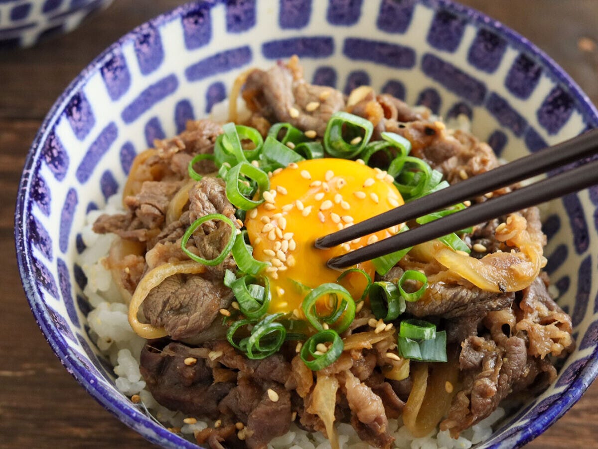 模様の丼のスタミナ丼に、黒い箸で中央の卵黄を崩そうとしている様子 模様の丼のスタミナ丼に、黒い箸で中央の卵黄を崩そうとしている様子