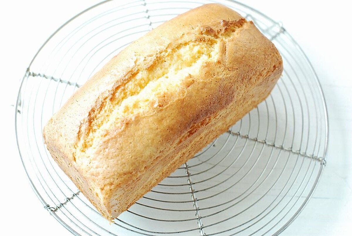 円形のワイヤーケーキクーラーに乗せたきつね色に焼き上がったヨーグルトレモンケーキの斜めアングル写真