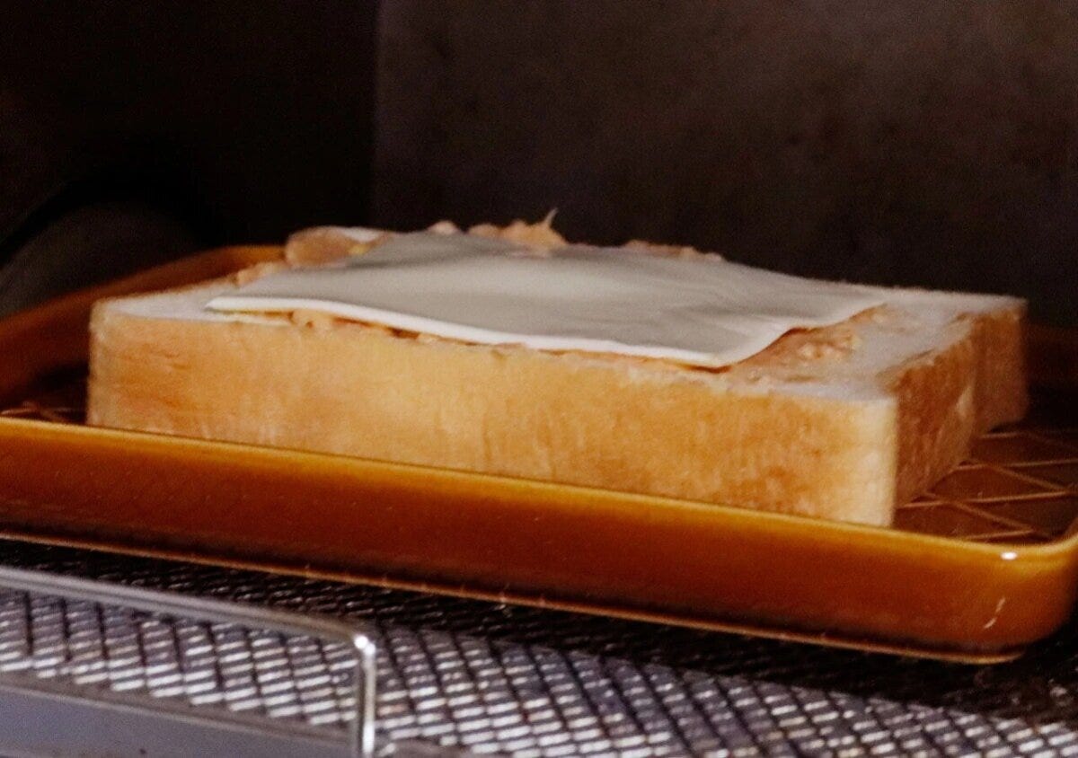 トースターの中で、茶色のトーストプレートに食パンとチーズが乗っている様子